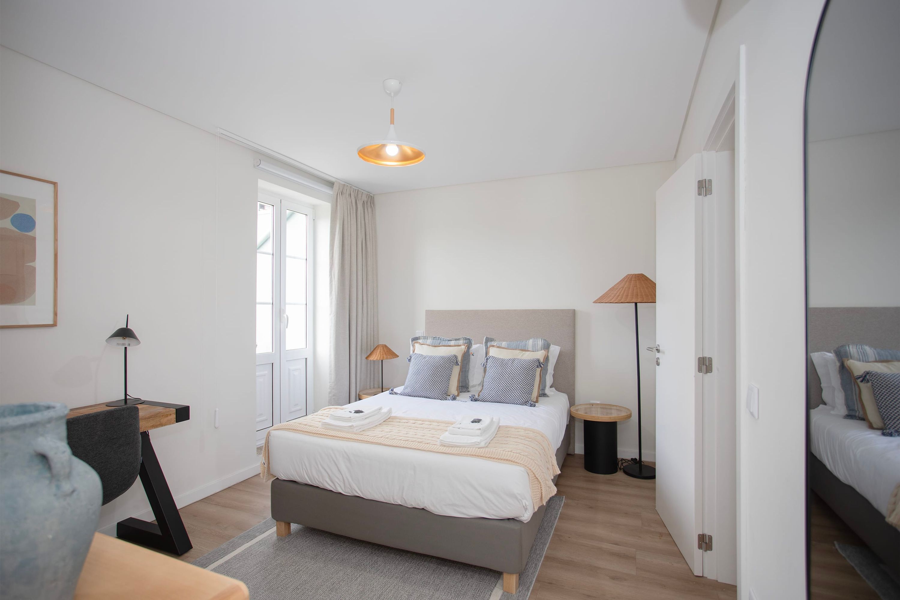 A modern bedroom with a bed, bedside tables, a desk, and a window.