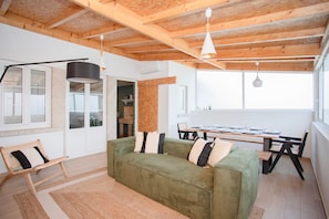 Una sala de estar moderna con un sofá verde, vigas de techo de madera y un comedor con una mesa y sillas.