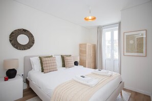 A modern hotel room with a large bed, a bedside table with a lamp, a circular wall decoration, a wardrobe, and a window with curtains. - Liiiving in Porto - Downtown Quiet House (Porto)