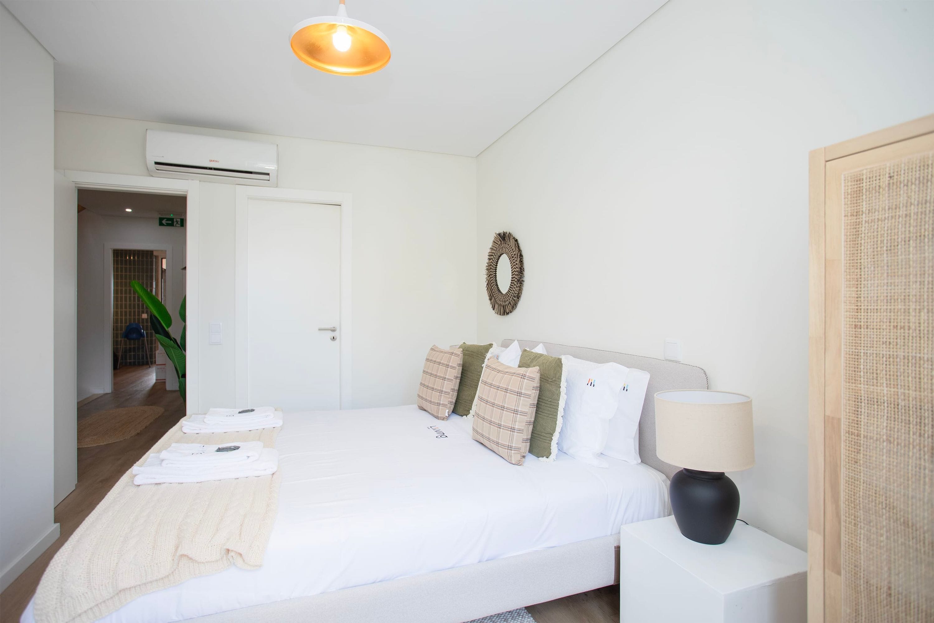 A neatly made bed with a white duvet, a bedside lamp, and a wall-mounted air conditioner.