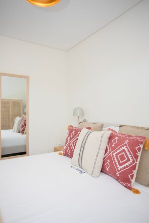 A neatly made bed with patterned pillows, a bedside lamp, and a mirror on the wall.
