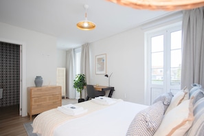 Una habitación de hotel moderna con una cama grande, un escritorio, una silla, una planta en maceta y una ventana con cortinas.