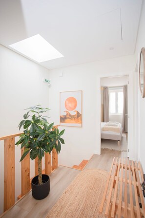 Moderni sisustus, jossa on kattovalokuvio, ruukussa oleva kasvi, kehystetty taideteos, sänky ja puinen penkki.