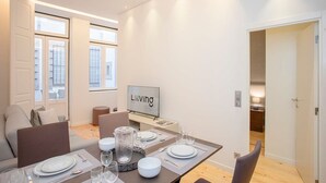 Et moderne spiseområde med et bord dækket til fire personer, et fjernsyn og udsigt over byen gennem store vinduer.