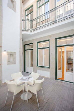 Un patio con una mesa y sillas, un balcón con baranda decorativa y una puerta que da a un espacio interior.
