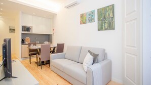 En moderne stue med en grå sofa, et fladskærms-tv og et spiseområde med stole og et bord.