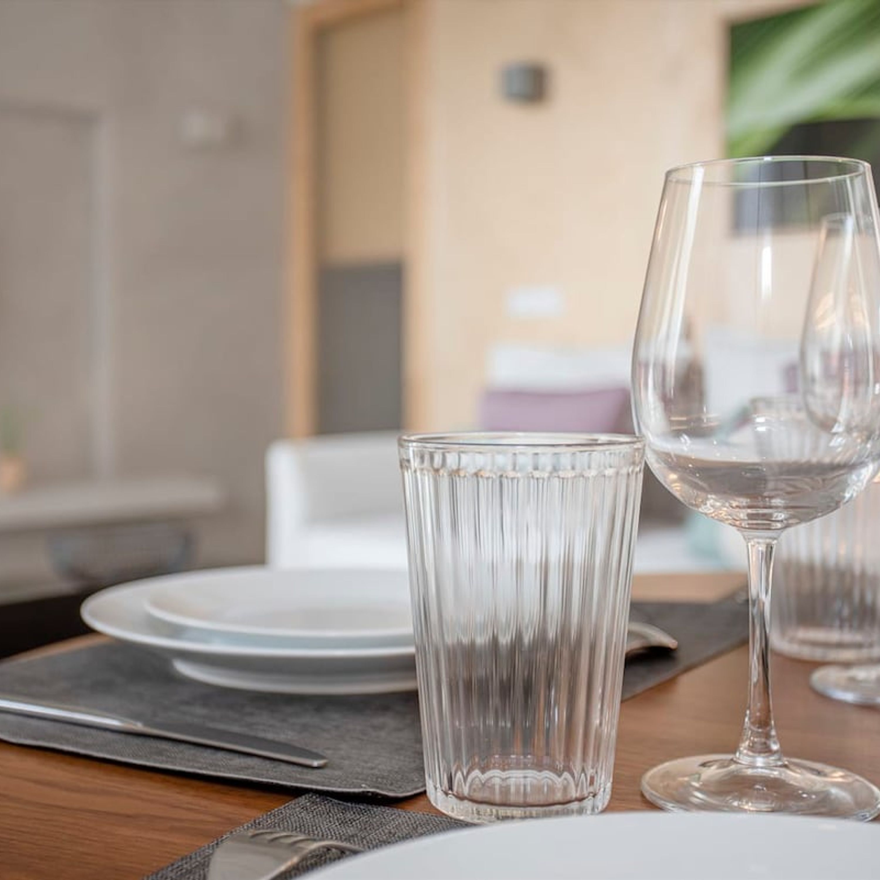 A dining table with a clear glass wine glass and a tall, ribbed glass.