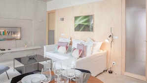 A modern living room with a white sofa, a dining table set for six, and a television on the wall. - Liiiving in Porto - Bolh o Trendy Apartment III (Porto)