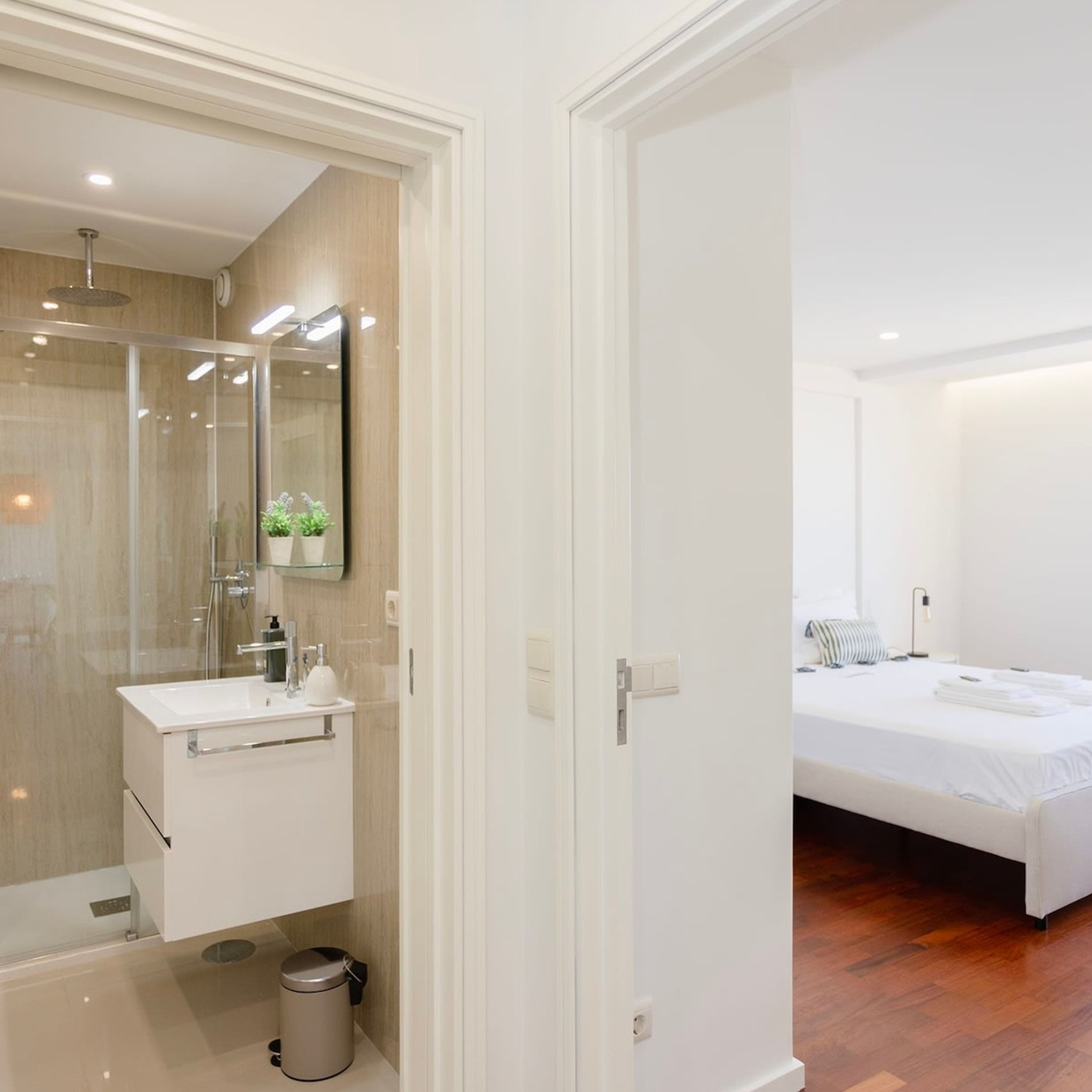 Un baño moderno con mampara de vidrio, tocador blanco y un pequeño cubo de basura.