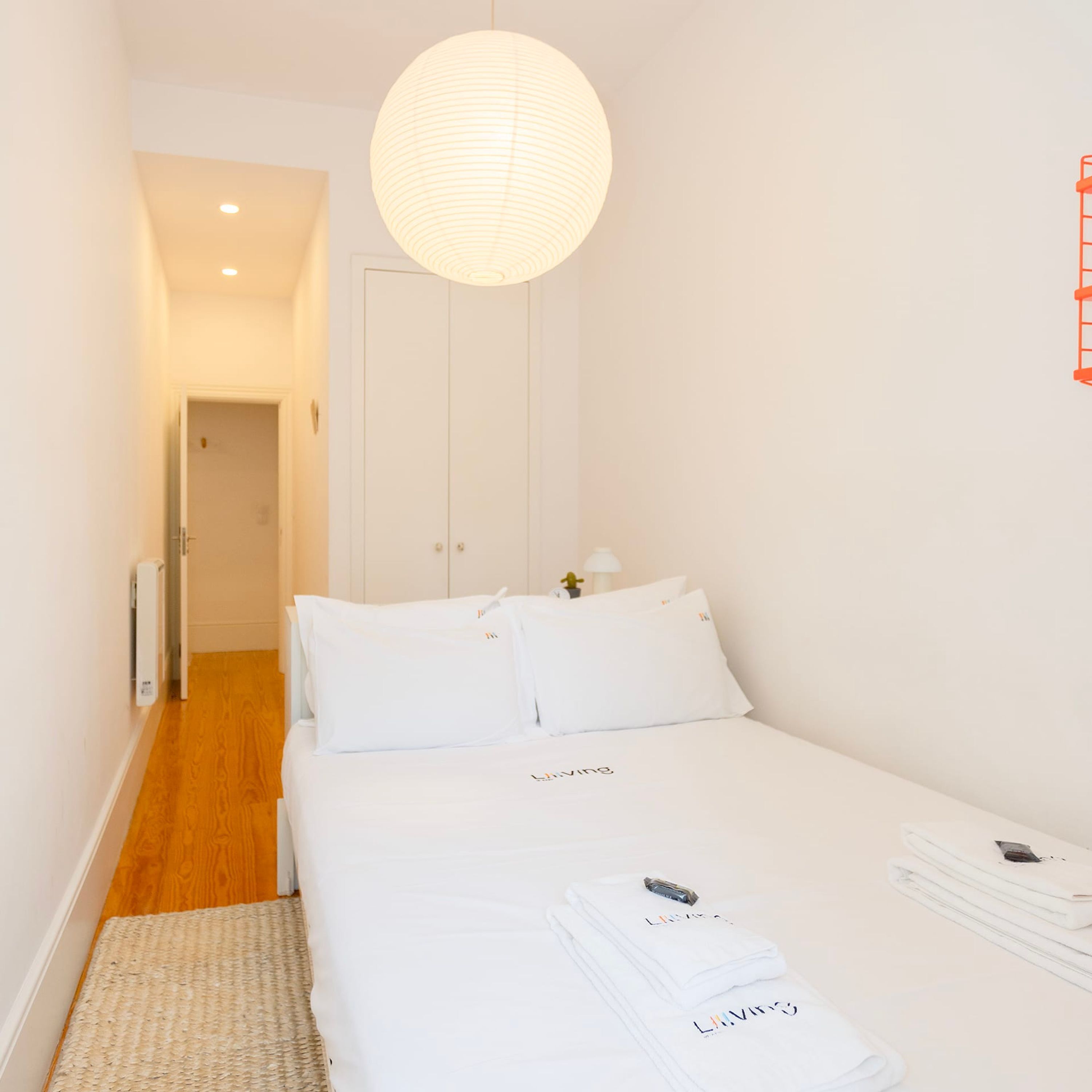 A hotel room with a neatly made bed, a hanging light fixture, and a door leading to another room.