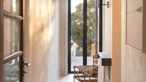 A narrow hallway with a door on the left, a wicker chair and table in the center, and a large window at the end. - Liiiving in Porto - Casa Duque Apartment II (Porto)