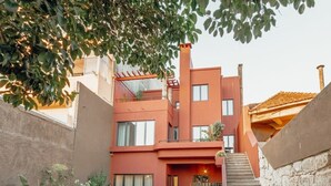 A modern building with a red facade, a courtyard with potted plants, outdoor seating, and a stone staircase. - Liiiving in Porto - Casa Duque Apartment II (Porto)