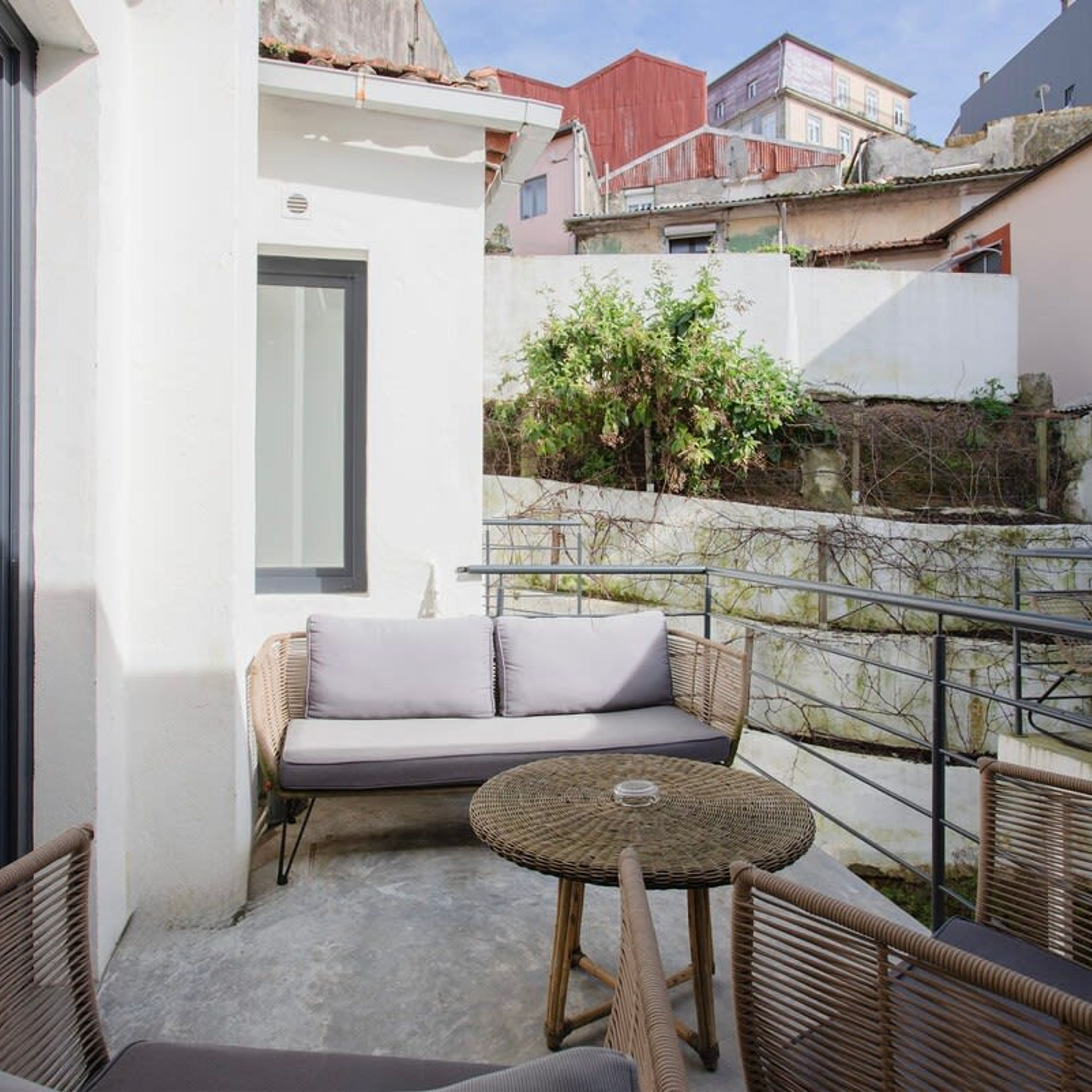 Un balcón con muebles de mimbre, una pequeña mesa y vistas a edificios cercanos.