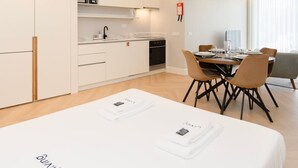 A modern hotel room with a large bed, a dining area with a table and chairs, a kitchenette, and a large window. - Liiiving in Porto - Luxury Design Apartment I (Porto)
