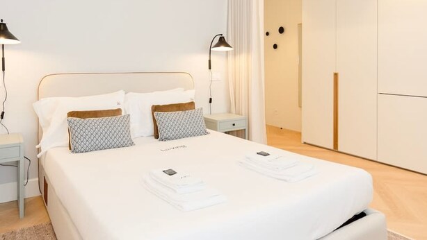 A modern bedroom with a large bed, bedside tables, a wardrobe, and a bathroom visible through an open door. - Liiiving in Porto - Luxury Design Apartment I (Porto)