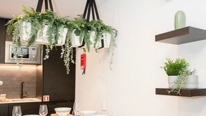 Une cuisine moderne agrémentée de plantes suspendues, une table à manger dressée pour quatre personnes et des étagères intégrées où sont disposées des plantes.