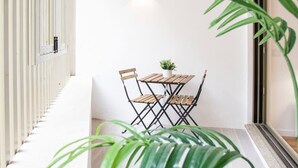 Un couloir étroit avec une petite table et des chaises, une plante en pot et une fenêtre avec des stores.