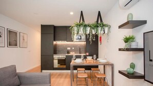 Une cuisine moderne avec des meubles de couleur sombre, un îlot central, des plantes suspendues et un coin repas équipé de tabourets.