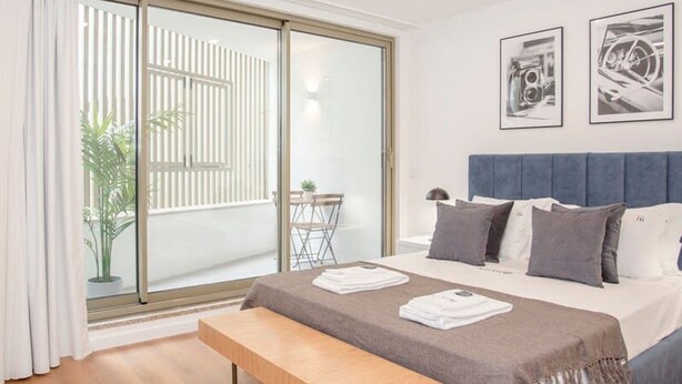 Une chambre moderne avec un grand lit, un banc et une porte-fenêtre coulissante donnant sur un balcon.