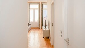 Un couloir étroit avec un plancher en bois, des murs blancs et une porte sur le côté droit.