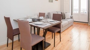 Un coin repas avec une table en bois dressée pour quatre personnes, un canapé et une grande fenêtre donnant sur un beau paysage.