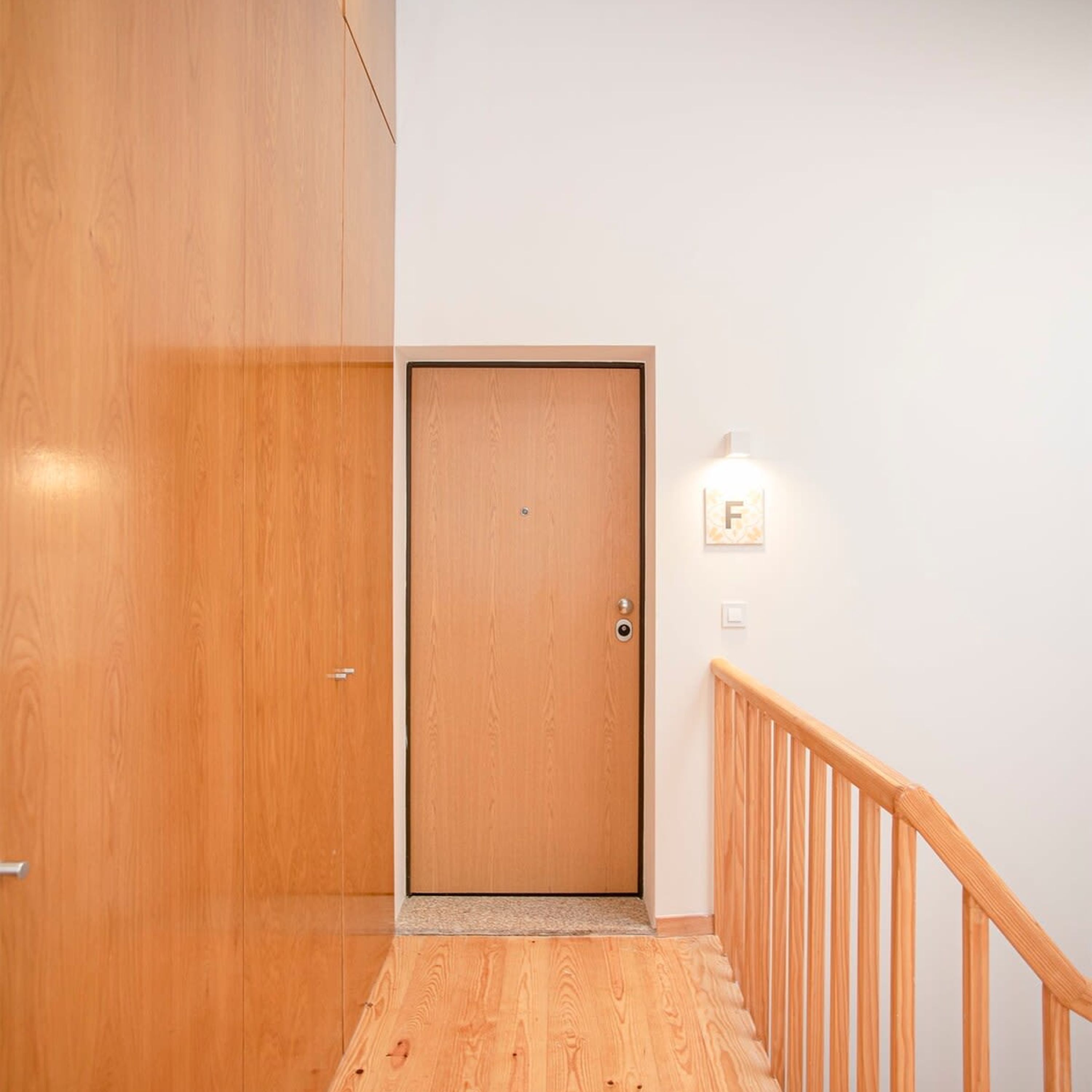 A wooden door with a handle and a keyhole, a wooden staircase with a handrail, and a light switch on the wall.