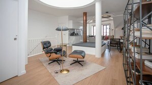 A spacious living area with a high ceiling, a central seating area with two chairs and a coffee table, a bookshelf, and a staircase leading to an upper level. - Liiiving in Porto - Ribeira Vintage View (Porto)