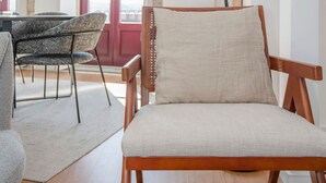 Un salon moderne avec un fauteuil en bois, un canapé gris et un lampadaire noir.