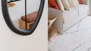 A room with a large oval mirror on the wall, a white sofa with cushions, and a wooden bench. - Liiiving in Porto - Mezzanine Delight Apartment (Porto)