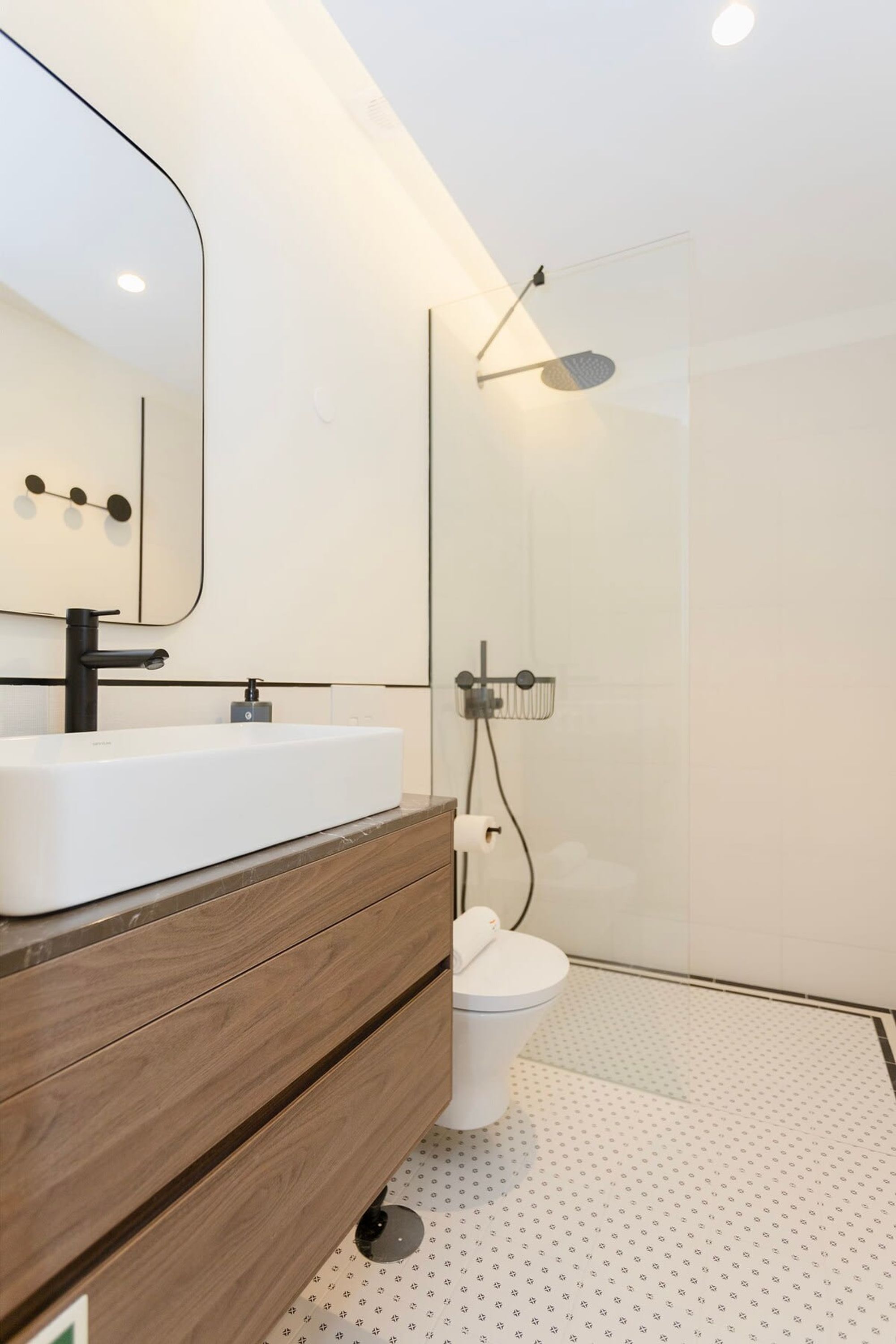 Een moderne badkamer met een wit wastafel, een spiegel, een houten wastafelmeubel, een toilet en een douchecabine met glazen wanden.