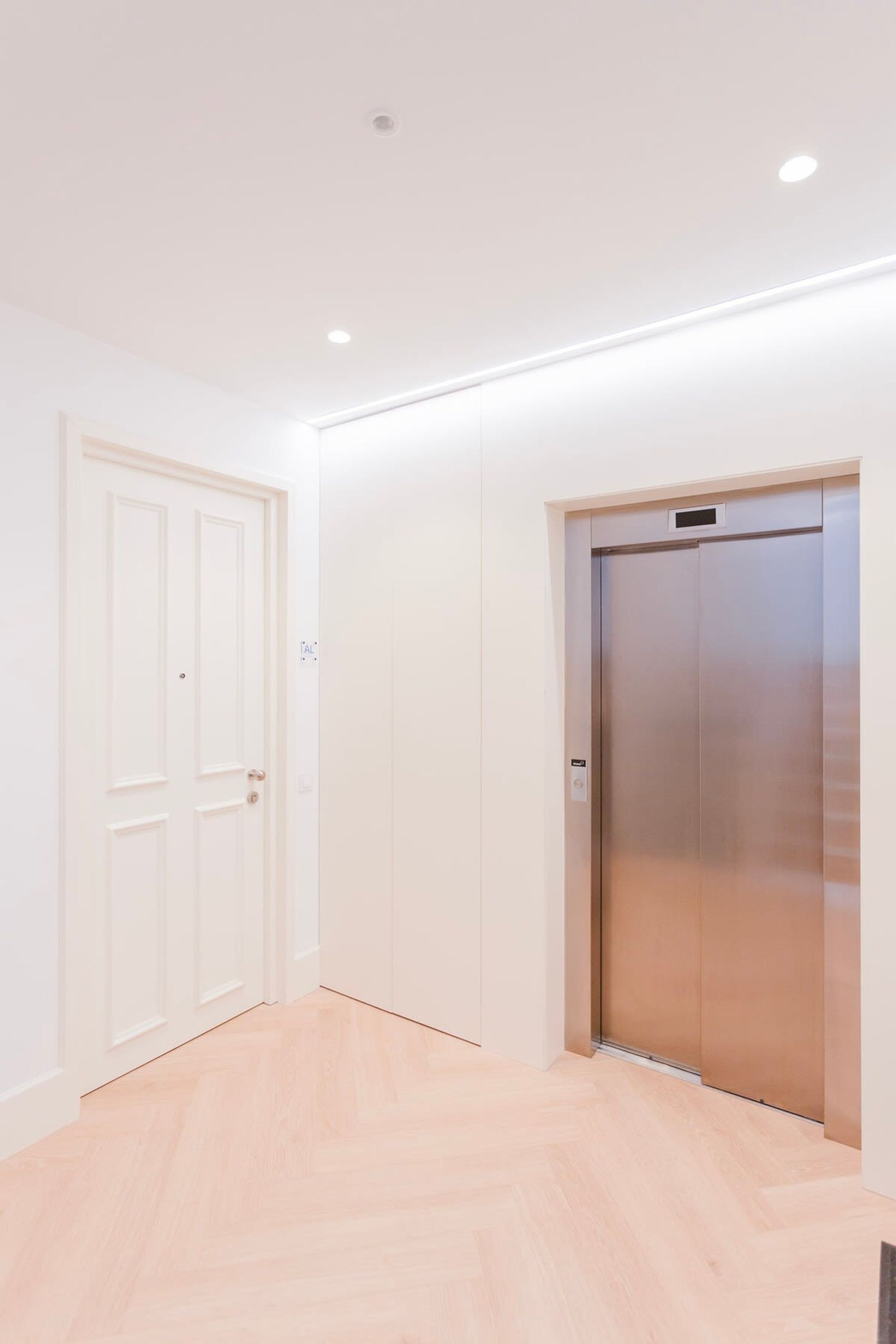 A modern interior with a wooden floor, a white door, and a metallic elevator.