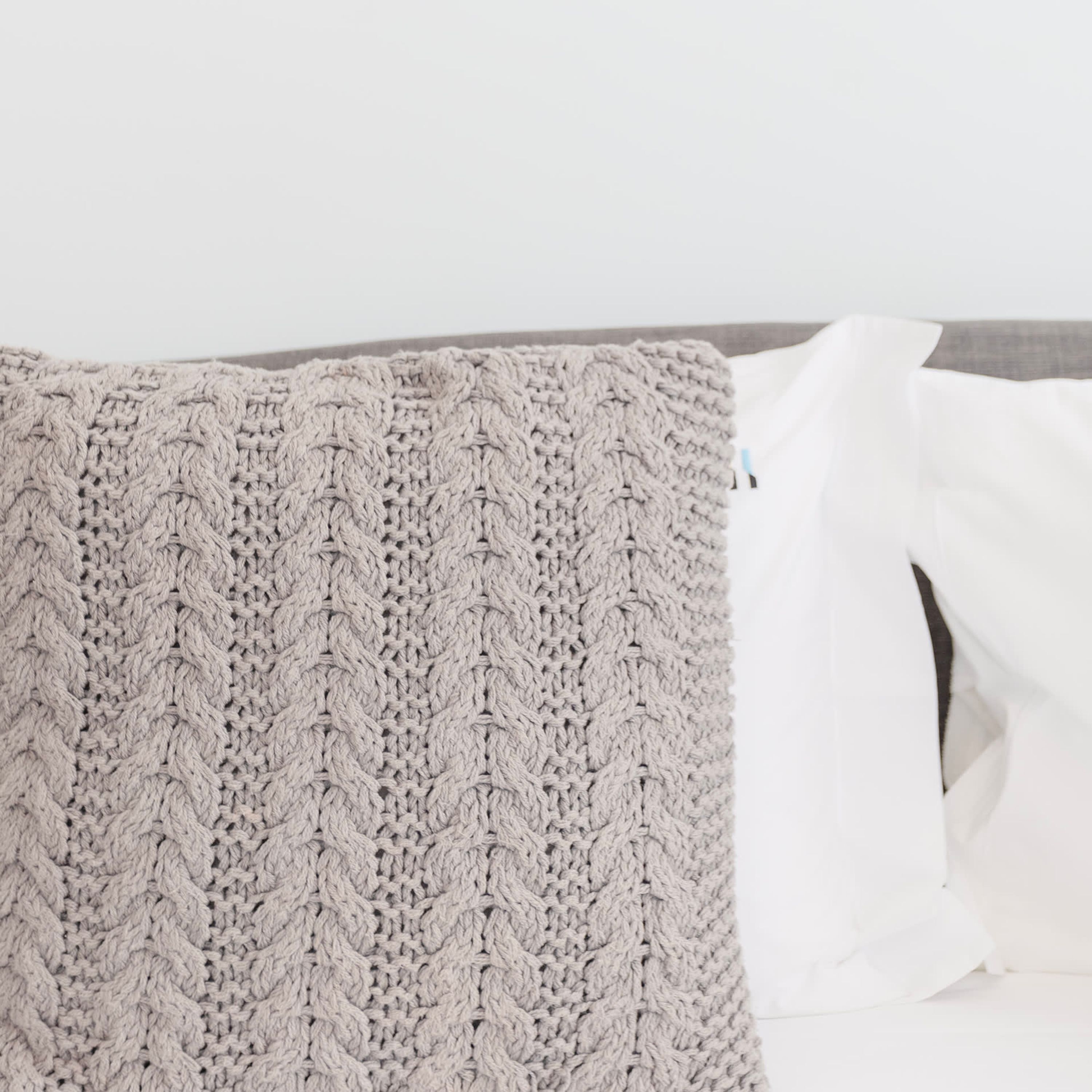 A knitted throw blanket with a cable knit pattern on a white sofa.