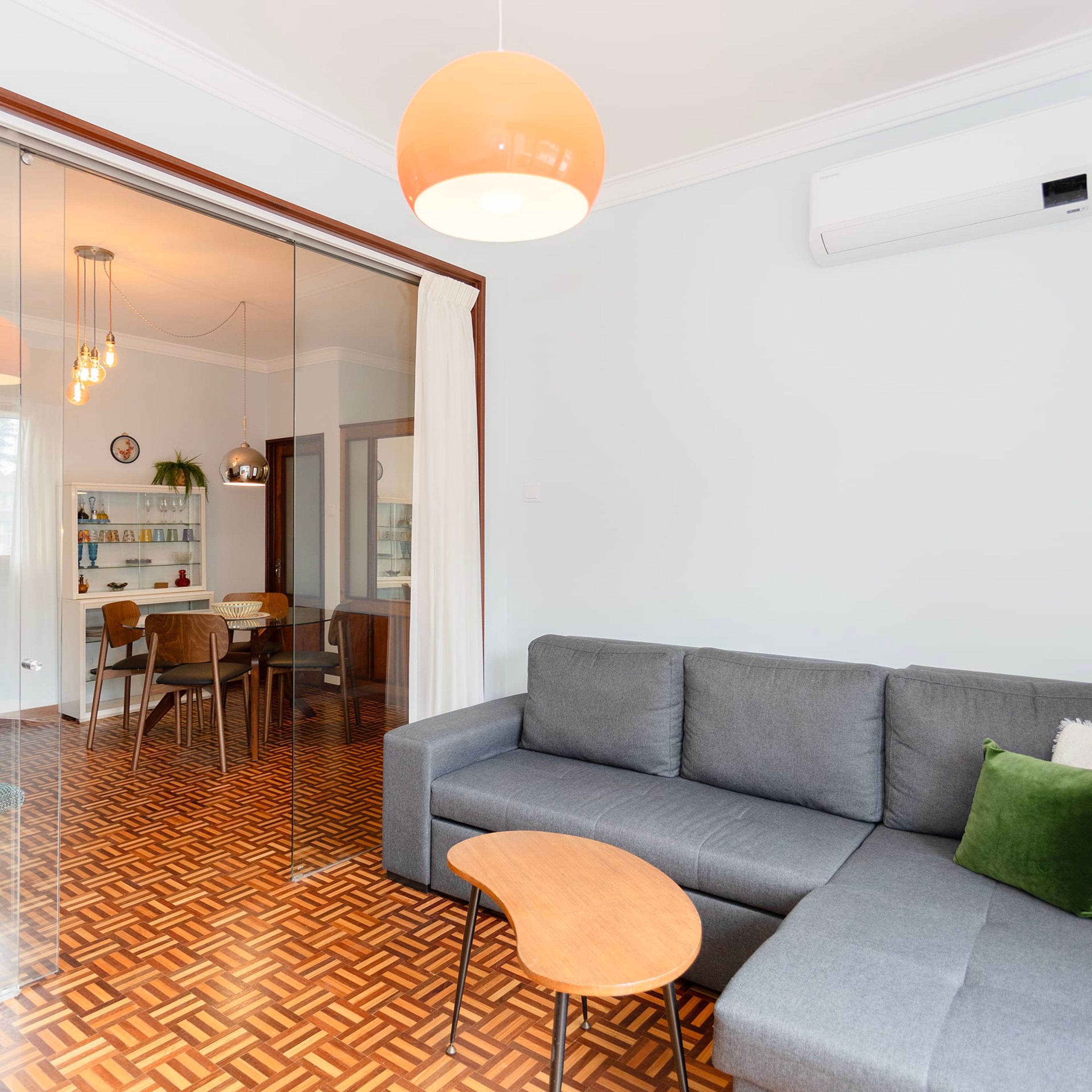 Een moderne woonkamer met een grijze bank, een houten salontafel en een visgraatvloer.