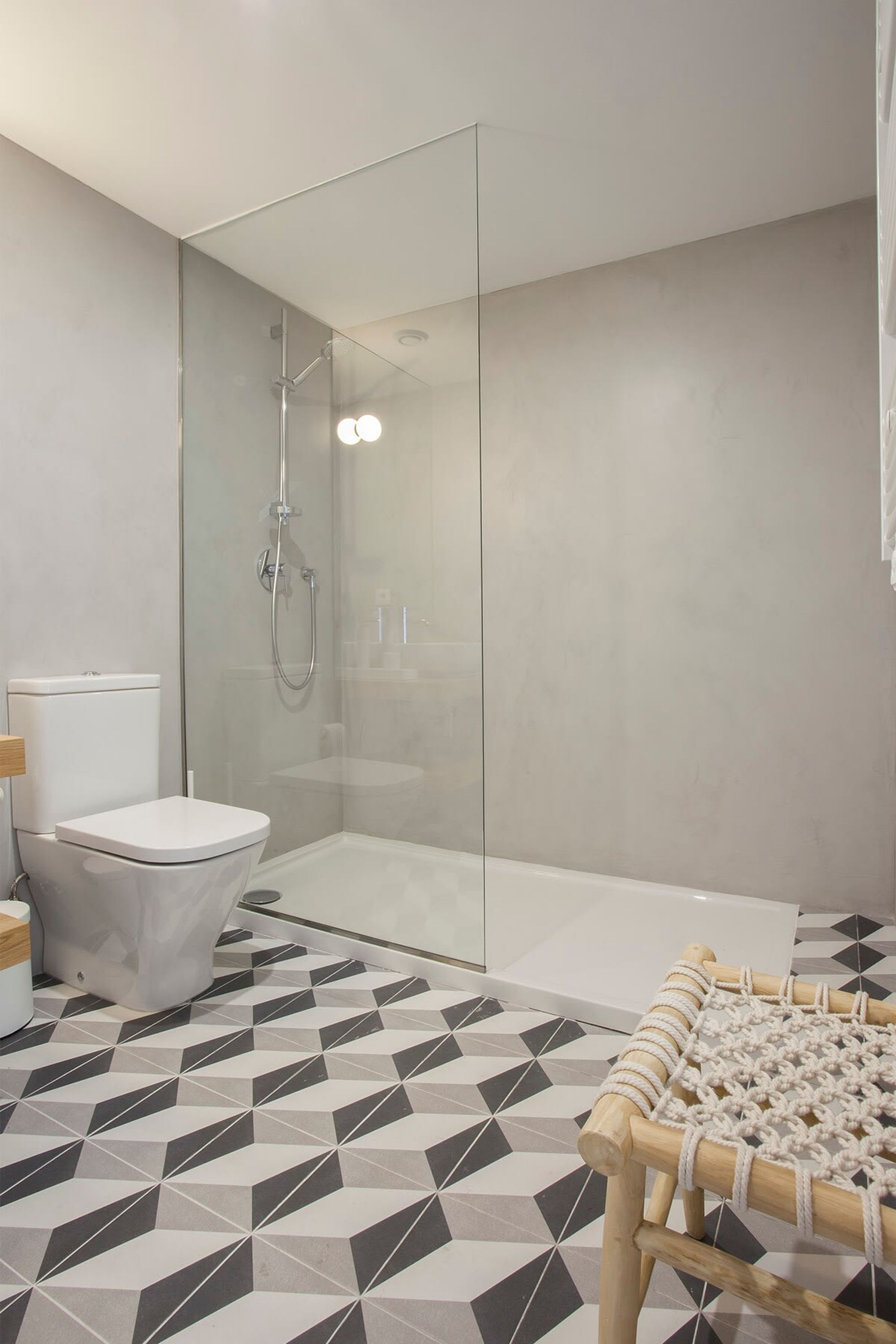 A modern bathroom with a glass-enclosed shower, a toilet, and a patterned floor.