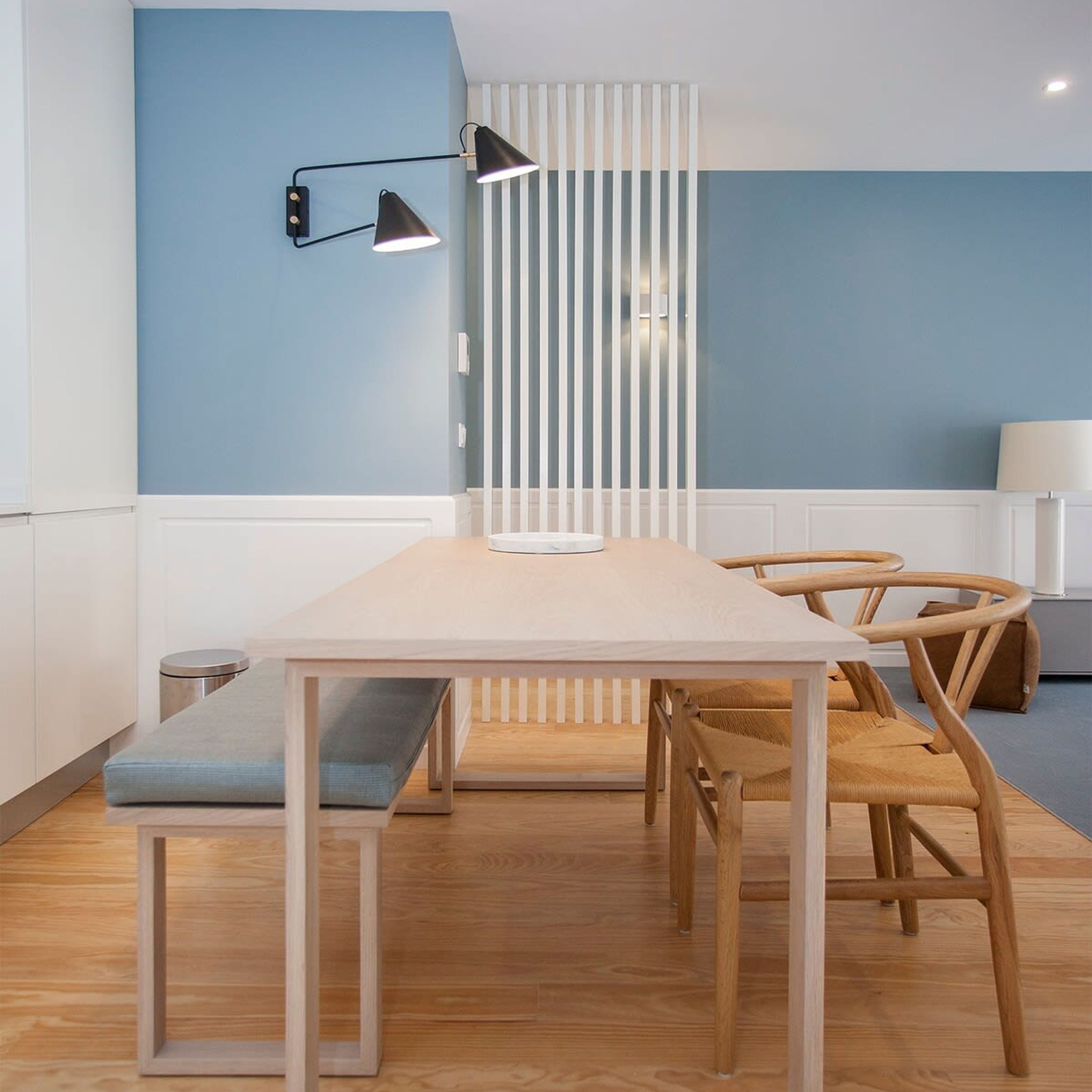 A modern dining area with a long table, wooden chairs, a bench, and a wall-mounted lamp.