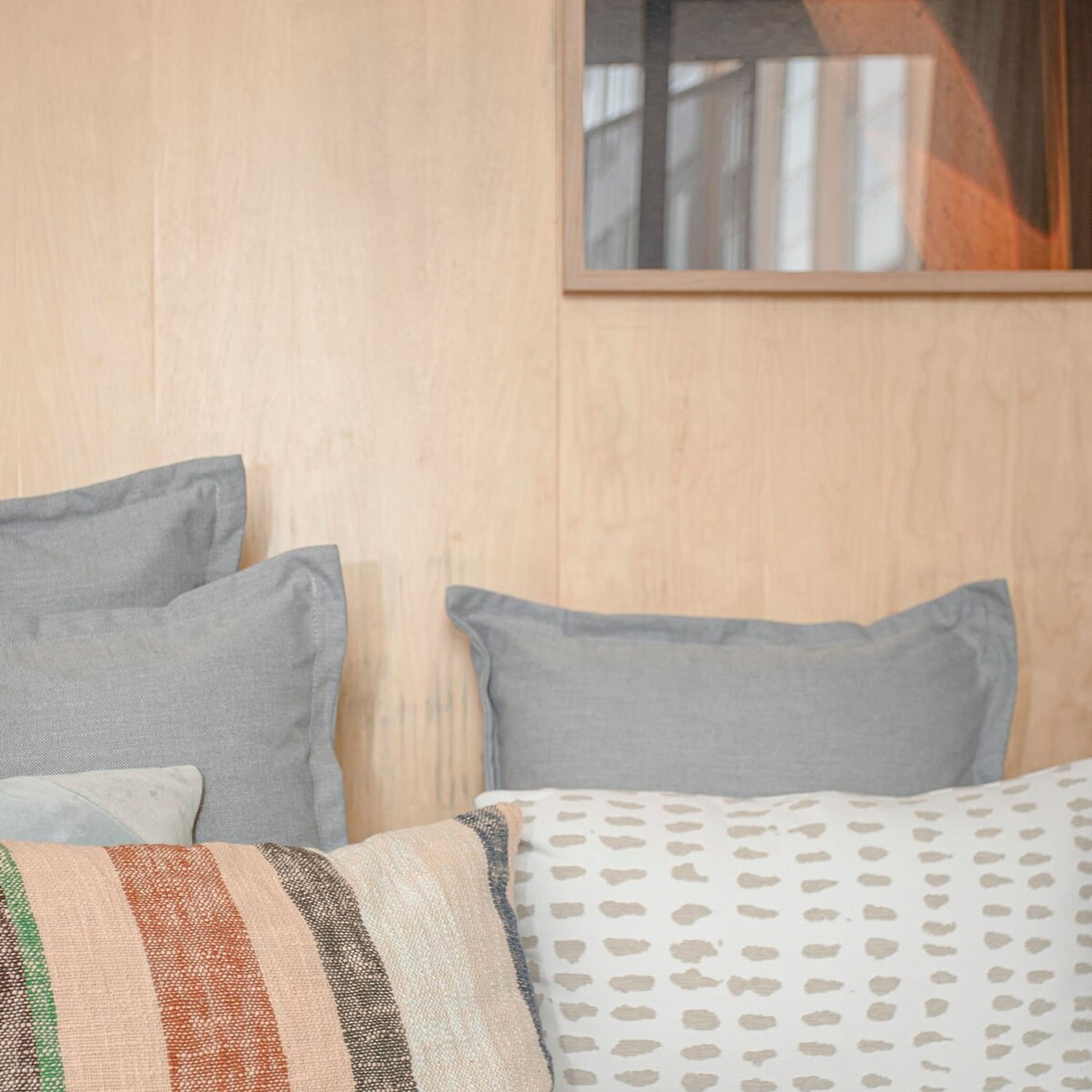 Un dormitorio con pared de madera, una cama con manta estampada y dos almohadas.