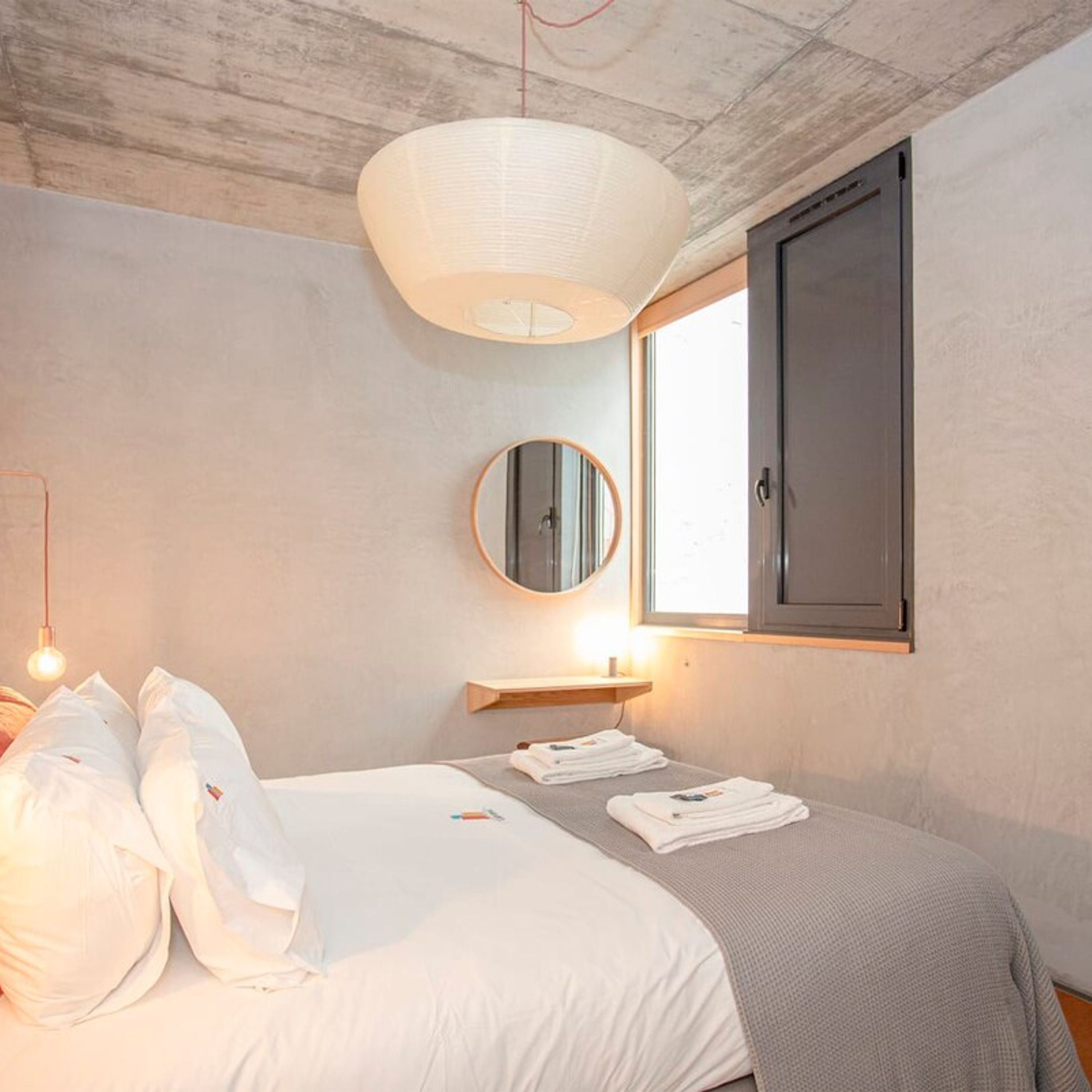 Een slaapkamer met een bed, nachtkastje, spiegel en raam.