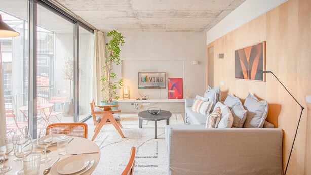 Un salon moderne avec un canapé, une table basse et un coin repas comprenant des chaises et une table dressée pour deux personnes.