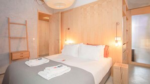 Une chambre d’hôtel avec un grand lit, une tête de lit en bois, des lampes de chevet, une table de chevet en bois et une fenêtre avec des stores.