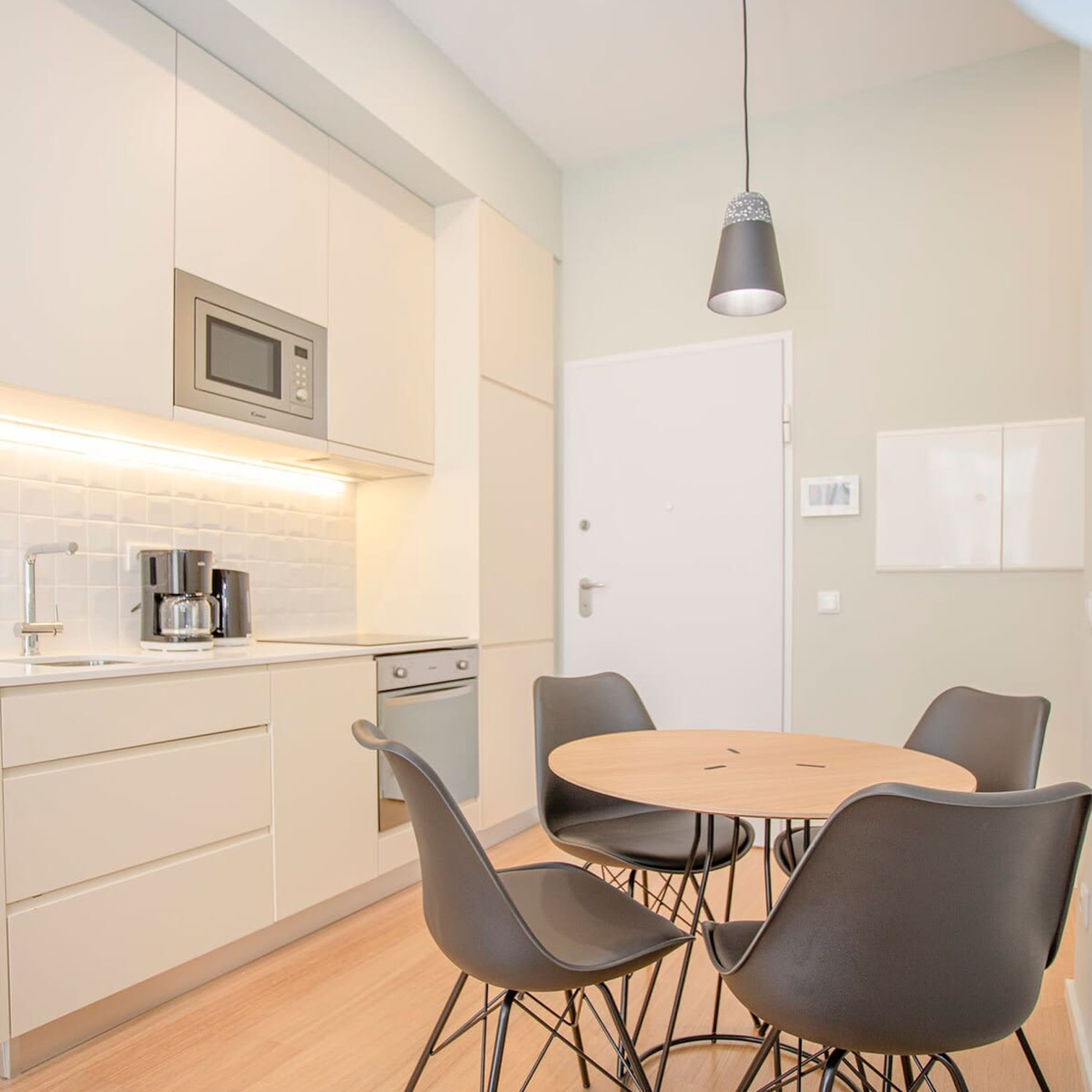 A modern kitchen with white cabinets, a microwave, a coffee machine, and a round dining table with four chairs.