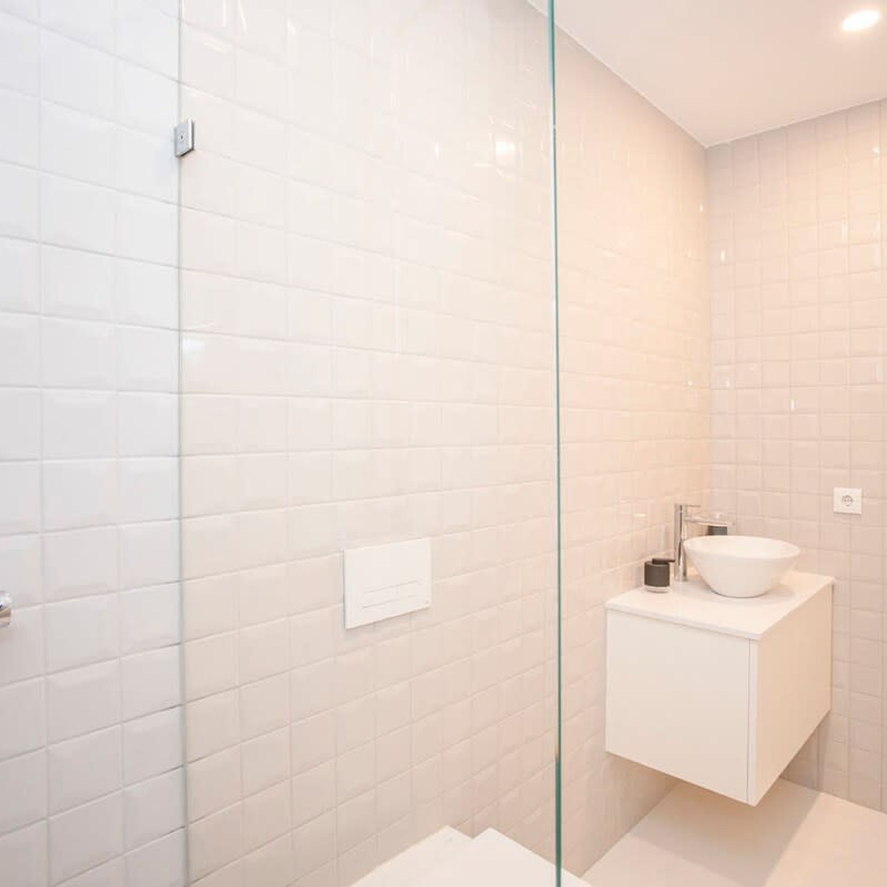 Une salle de bain moderne avec des carreaux blancs, une douche en verre et un lavabo blanc au design minimaliste.