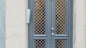 Une porte à deux battants ornée d’un motif en treillis, une boîte aux lettres et une petite grille d’aération dans le mur.