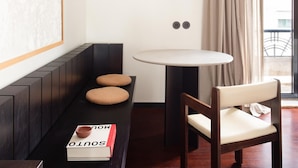 A corner room with a dark wooden bench, a round table, and a chair. There is a book titled "SOUTO" on the bench. - Liiiving in Porto - Casa Duque Apartment IV (Porto)