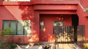 A modern red building with multiple windows, a balcony, and a small garden area with plants and a barbecue grill. - Liiiving in Porto - Casa Duque Apartment IV (Porto)