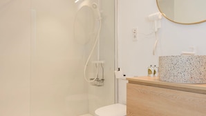 Ein modernes Badezimmer mit einer gläsernen Duschkabine, einer weißen Toilette, einem hölzernen Waschtisch mit Marmorplatte und einem runden Spiegel.