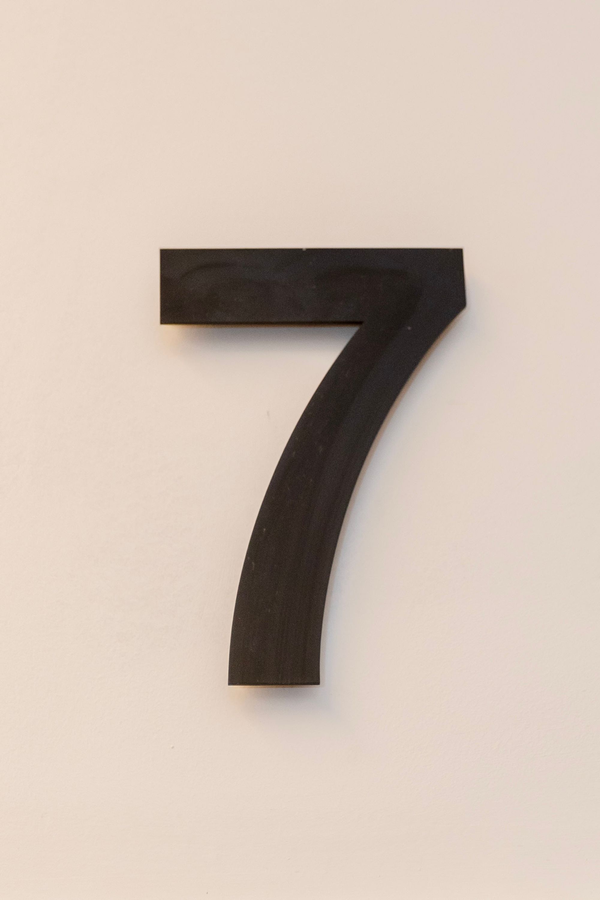 Un chiffre 7 noir, en relief, sur un mur uni.