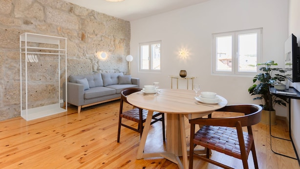 Ein modernes Wohnzimmer mit Steinwand, einem grauen Sofa, Holzboden, einem runden Esstisch mit Stühlen und einer hängenden Leuchte.