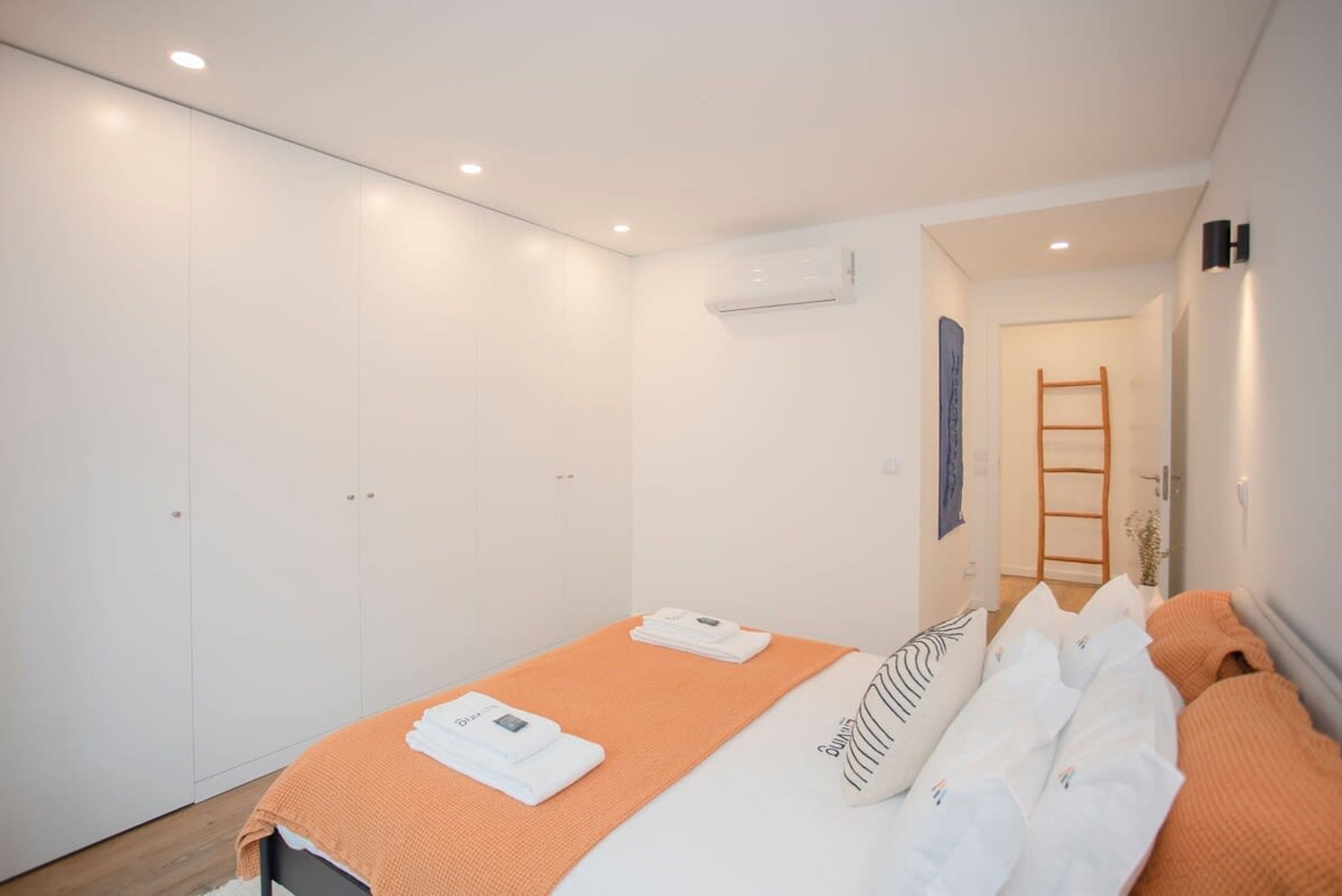 A modern bedroom with a bed, a wardrobe, and an air conditioning unit.