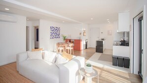 En moderne stue med en hvid sofa, et spisebord, et køkken og en lille altan.
