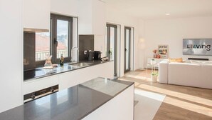 Et moderne køkken med en stor ø, et spiseområde med en hvid sofa og et fjernsyn ophængt på væggen.